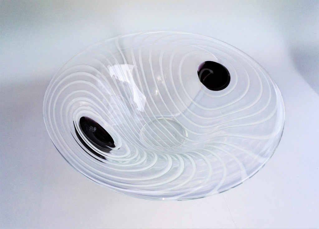 Kirkkaasta lasista hyttityönä suupuhaltamalla valmistettu uniikkilasivati. Lasinen aloituspallo on puhkaistu sivusta happiliekillä ja kiinnitetty puntteliin sivusta. Vadin aukaisu on tapahtunut sivukiinnityksessä pallomuodosta käyttäen puhkaistua aukkoa. Heikki Jylhä-Vuorio.