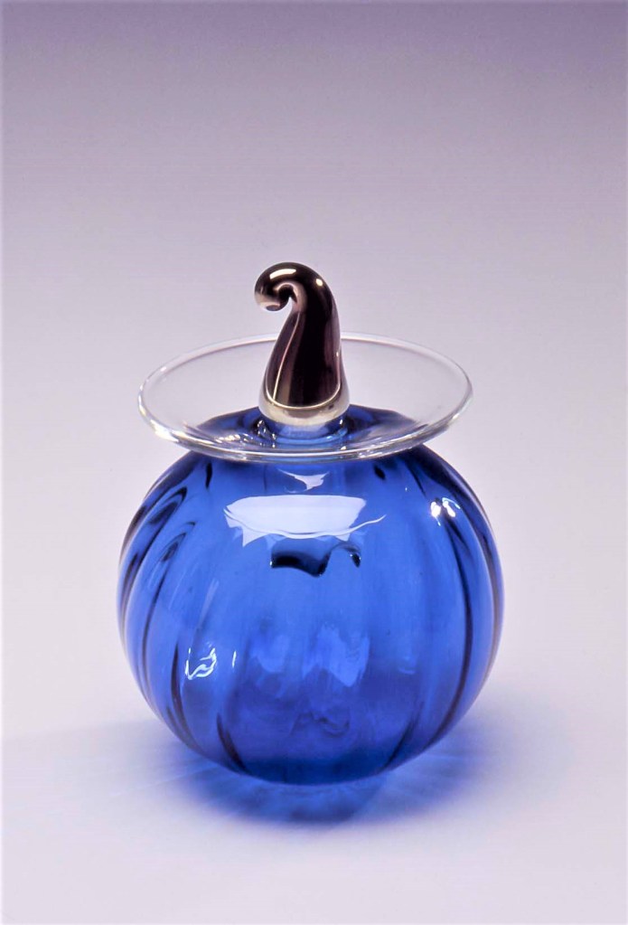 Hyttityönä puhallettu sininen lssinpuhallus työ, uniikkilasi maljakko nimeltään Kevätverso, korkin yläosa on lysteripintainen. Koristelu on tehty filigraanitekniikalla. Heikki Jylhä-Vuorio.