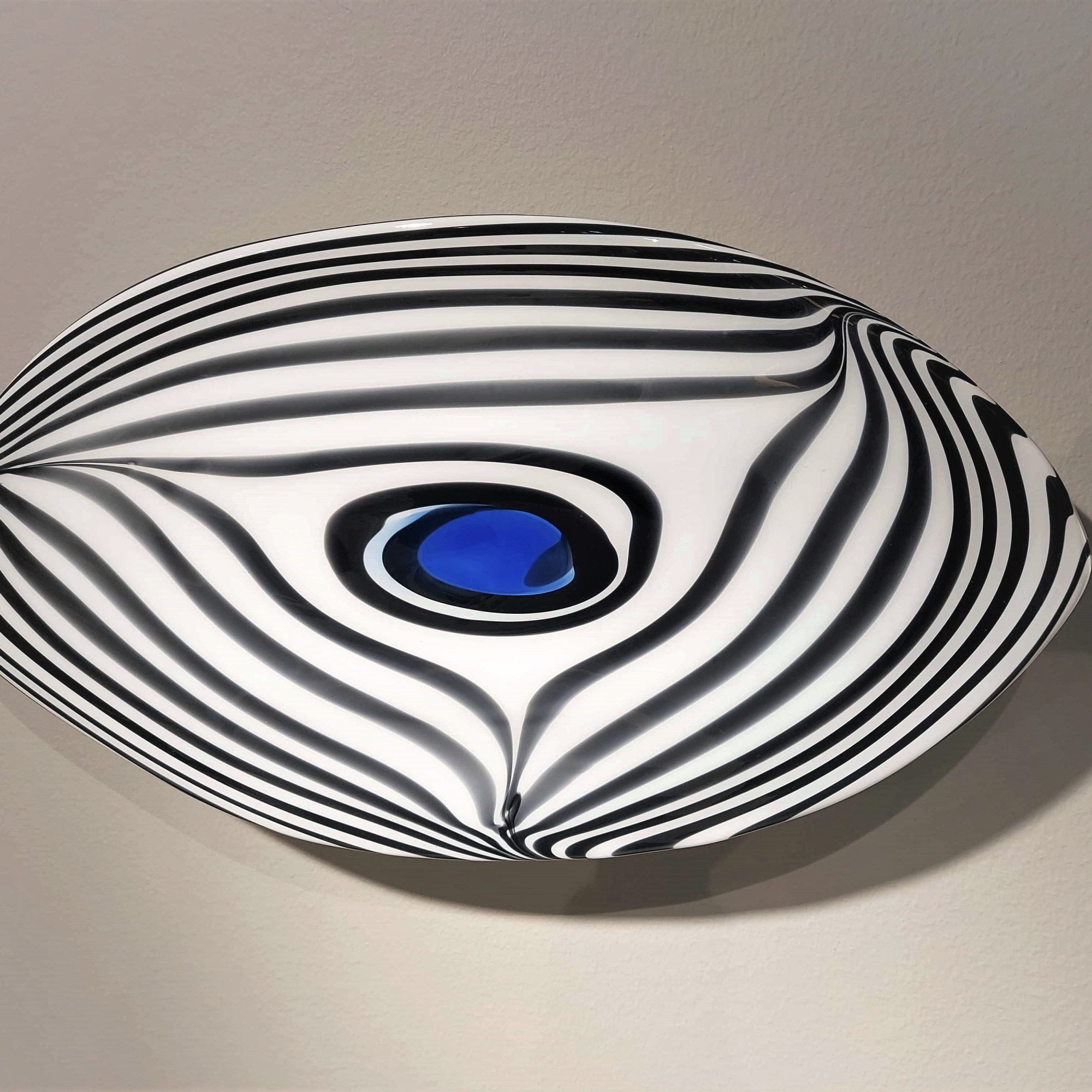 Siipimäinen, hyttityönä suupuhallettu lasinen uniikkiveistos nimeltään Sukellus kiinnitettynä seinään takaosassa olevan metallitelineen avulla. Heikki Jylhä-Vuorio.